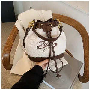 Detail of plush bucket bag with cream fleece fabric, brown leather straps, and embroidery