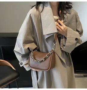 Sac hobo marron avec chaîne dorée porté par un mannequin en trench-coat beige