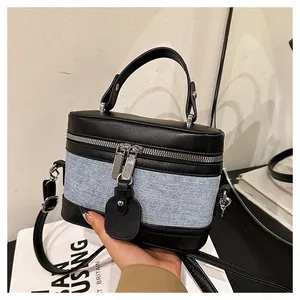 Detail of leather and denim bucket bag showing silver zippers and textured stitching