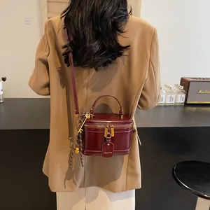 Detail of burgundy box bag with gold hardware and logo tag on a model in retro style