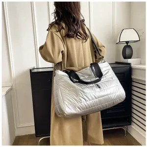 Dettaglio di una grande borsa trapuntata argento indossata da una modella in trench beige