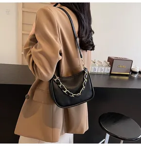 Détail d'un sac à bandoulière en cuir noir grainé avec une grosse chaîne dorée