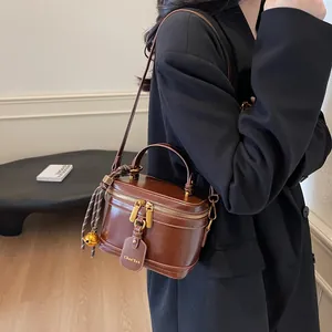 Detail of vintage brown leather box bag with dual zippers and golden bell charm accessory