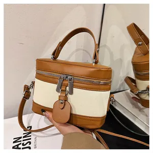 Detail of a brown and beige two-tone bucket bag with metal zippers and leather pendant