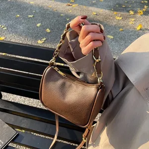 Sac Boston marron avec texture litchi et chaîne dorée sur un banc de parc