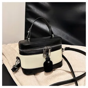 Detail of contrast stitching on a black leather and beige canvas bucket crossbody bag