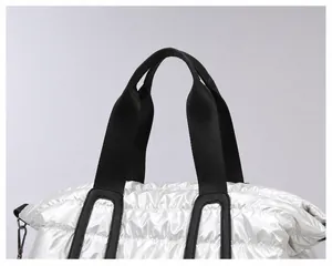 Detail view of silver quilted tote bag with smooth glossy fabric and black handles