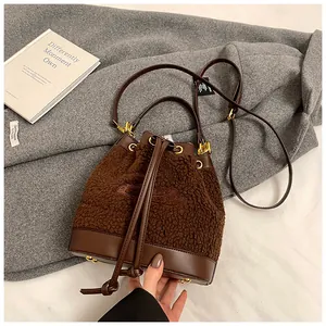 Detail of plush bucket bag with leather trim and gold hardware on grey coat