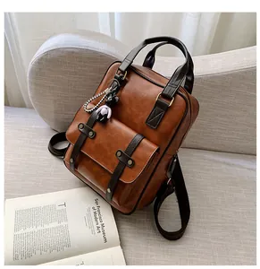 Detail view of vintage brown leather backpack with front flap and bear charm on sofa