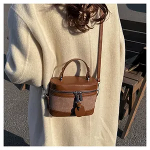 Detail of canvas and brown leather bucket bag showing stitching and silver zippers