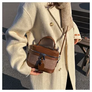 Brown leather-fabric mixed bucket bag shown on a beige wool coat in sunlight
