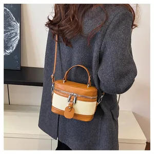 Detail of a brown leather and beige canvas crossbody bucket bag with silver zippers