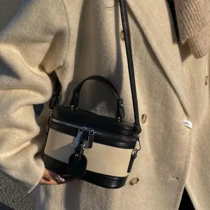 Minimalist black leather and beige canvas bucket bag with elegant metal zipper closure