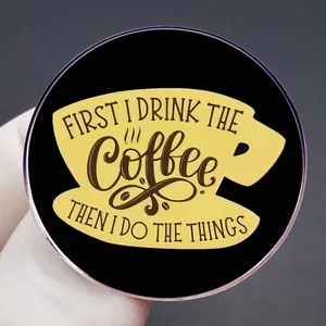 Round enamel pin with 'FIRST I DRINK THE Coffee' quote on black background
