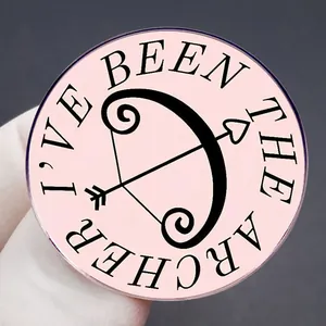 Pink I'VE BEEN THE ARCHER enamel pin with black bow and arrow motif on dark background