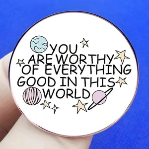 Broche ronde avec motifs célestes et citation inspirante en anglais sur fond blanc pur