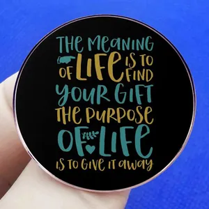 Runde Anstecknadel mit Motivationsspruch, roségoldener Kante, gehalten vor blauem Hintergrund