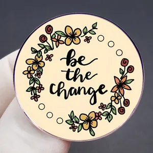 Round floral metal brooch badge with 'be the change' motivational English slogan