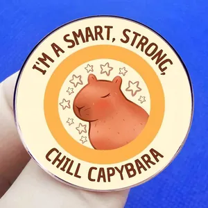Round metal capybara badge featuring cartoon art and motivational text on blue background