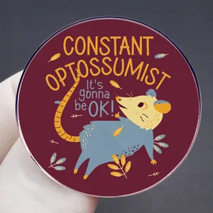 Round opossum enamel pin with Constant Optossumist text on a dark red background