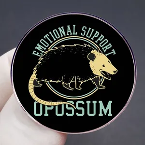 Round black enamel pin featuring emotional support opossum illustration and bold text