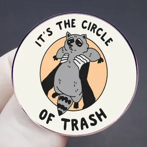 Round raccoon badge with It's The Circle Of Trash text held in hand against grey background