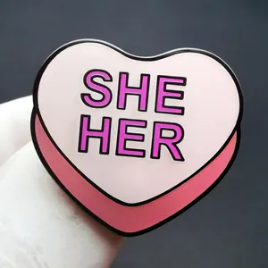 Spilla smaltata a cuore rosa con testo SHE HER e bordi in metallo nero