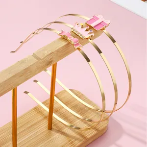 Detail von drei goldenen Haarreifen mit rosa Emaille-Schleife auf einem Holzständer