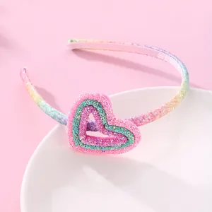 Rainbow glitter girls headband with heart decoration on a white ceramic plate
