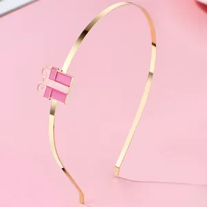 Detailaufnahme eines goldenen Haarreifs mit einem rosa Emaille-Geschenkbox-Anhänger