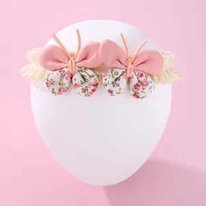 Bandeau bébé en dentelle florale avec nœuds roses présenté sur un support d'exposition