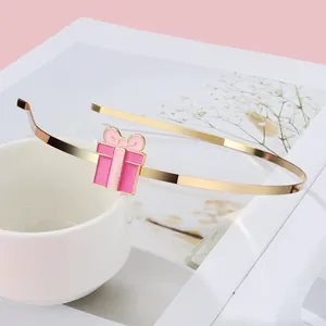 Detailansicht eines schmalen goldenen Haarreifs mit rosa Emaille-Geschenkbox-Verzierung