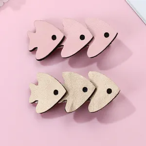 Detail of glittery fish-shaped hair clips in pink and gold with textured faux leather