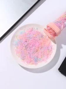 Pastel color elastic hair ties pouring from a pink storage tube onto a white plate