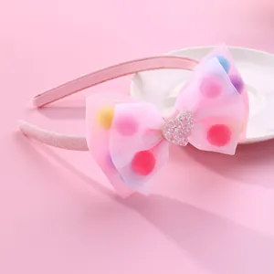 Detailed view of pink mesh bow headband with colorful pom-poms and glitter heart decoration
