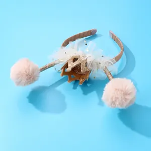 Dettaglio di cerchietto per bambini con corona dorata, tulle bianco e pompon rosa su molle