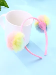 Détail d'un serre-tête rose avec des pompons en peluche arc-en-ciel sur une tasse