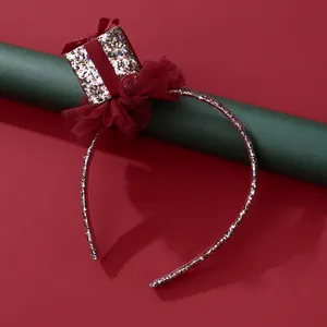 Detail of glitter Christmas headband featuring a red mesh bow and small gift box decoration