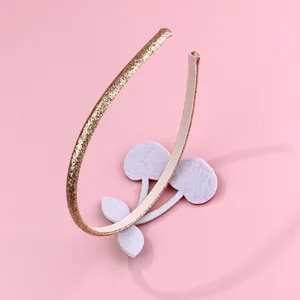 Detail of glittery gold headband with white cherry felt applique on pink background