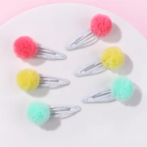 Détail de six barrettes BB scintillantes avec pompons en tulle colorés sur plat blanc