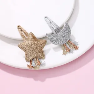 Détail de barrettes à paillettes en forme d'étoile et lune avec pompons sur fond pastel