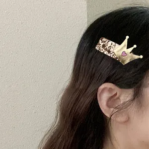 Detail of a gold sequin crown hair clip with pink hearts worn by a child model