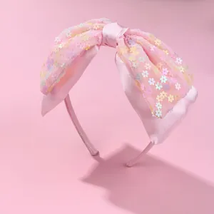 Detail of pink satin headband featuring a layered mesh bow with colorful flower sequins