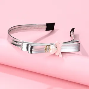 Detail of silver metallic headband featuring a fabric bow with golden crown and heart charm