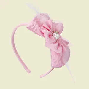 Detail of pink bow headband with soft white feathers and a tiny gold crown on heart charm