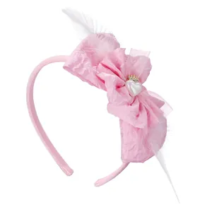 Pink glitter headband for girls with a large fabric bow, white feathers, and a gold crown heart
