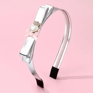 Detailed shot of silver bow headband with pearl heart and crown on a pink surface