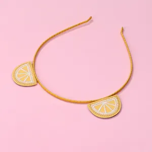 Detail of yellow fabric headband featuring embroidered lemon slices on a pink background