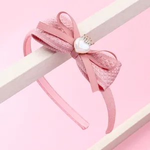 Détail du serre-tête avec nœud en tweed rose, cœur en résine et couronne dorée scintillante