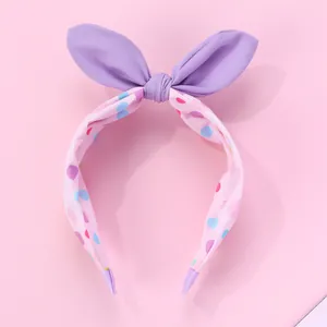 Détail d'un serre-tête oreilles de lapin violettes avec pois colorés sur tissu rose